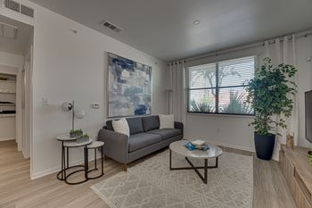 A living room with a grey couch, a small table with a plant on it, and a large painting on the wall.